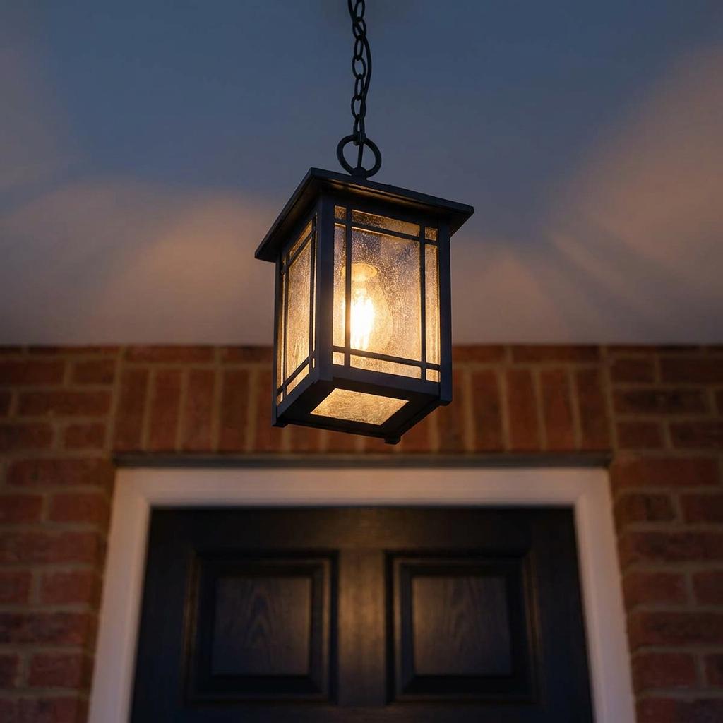 Cedar Point black outdoor chain lantern with seeded glass panels glowing warmly outside a brick house.