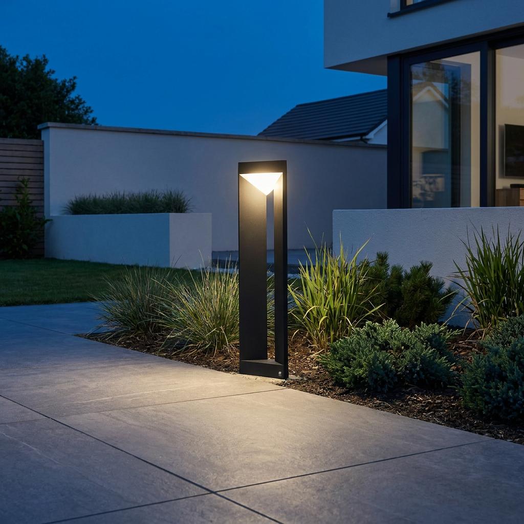 A black linear LED bollard light illuminates a stone pathway in a modern garden setting at twilight.