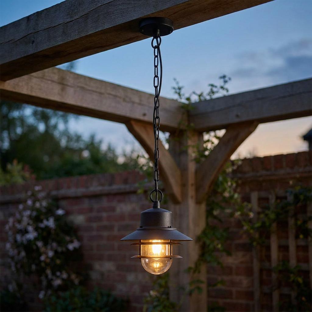 Elstead Copenhagen black outdoor chain lantern hanging from a wooden pergola beam at dusk.