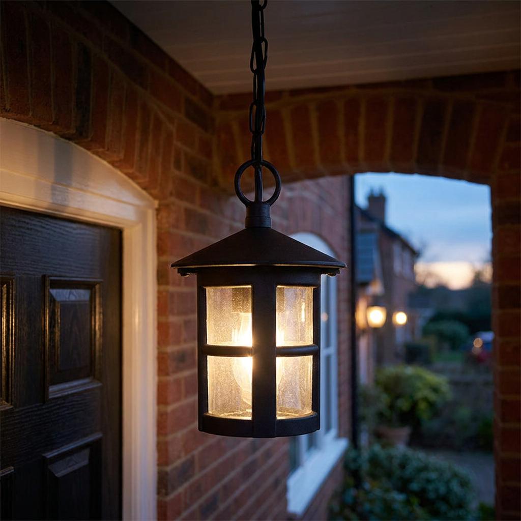 Black outdoor pendant lantern with textured glass glowing under a brick porch at twilight.