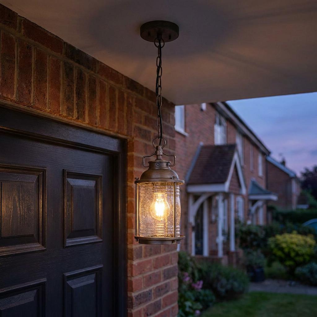 Illuminated bronze outdoor chain lantern with seeded glass hanging on a brick porch at twilight.