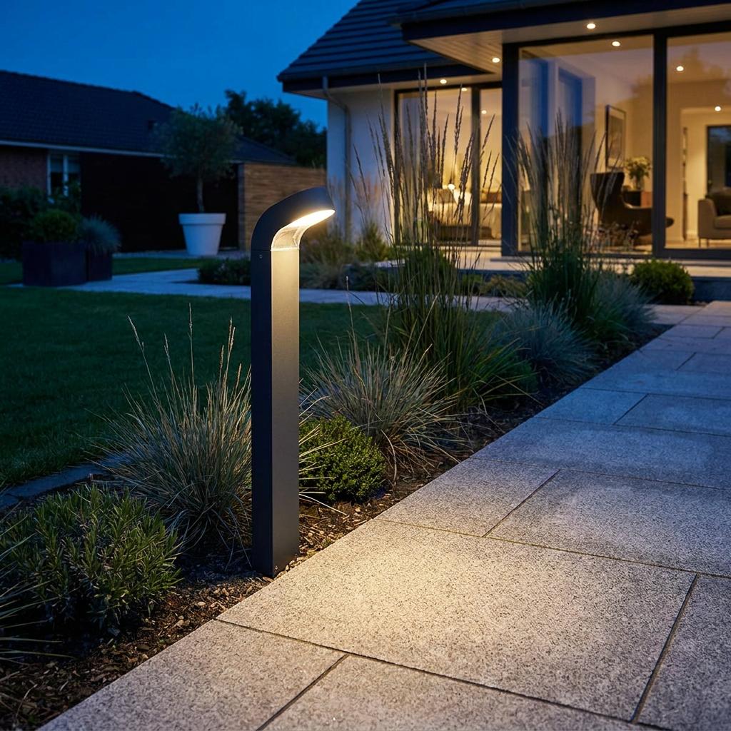 A graphite LED bollard light illuminates a stone pathway in a modern garden at twilight.
