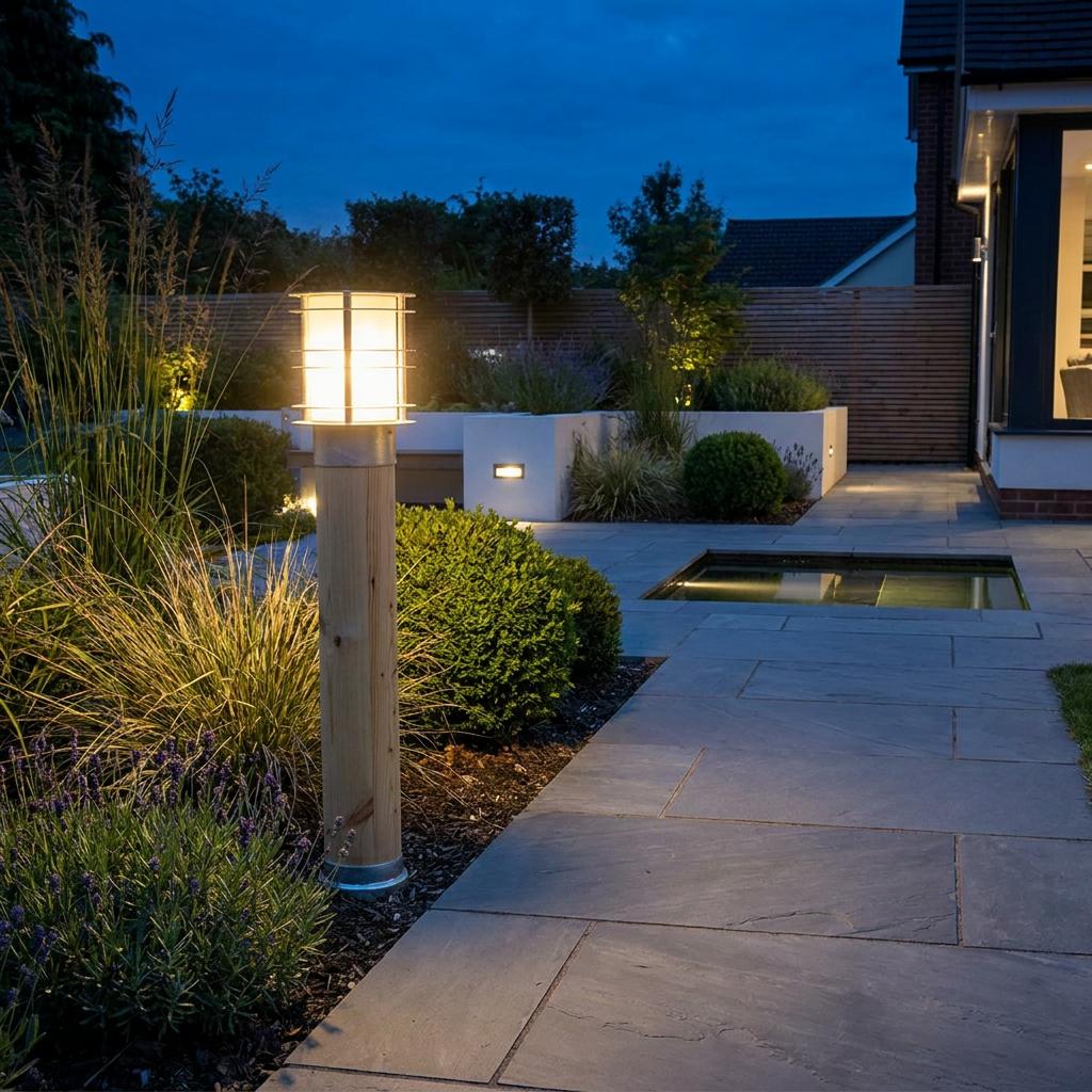 A glowing wood and galvanized steel bollard light illuminates a modern stone patio garden at dusk.