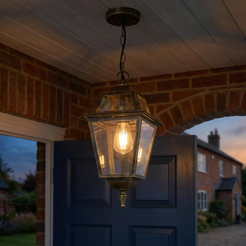 Black and gold outdoor pendant lantern with clear glass panels hanging from a porch ceiling lit at dusk.