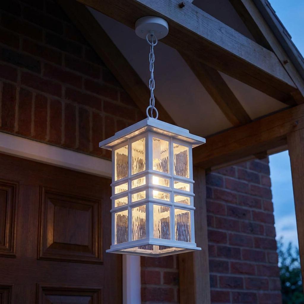 White outdoor chain lantern with hammered glass hanging from a wooden porch beam against a brick house at dusk.