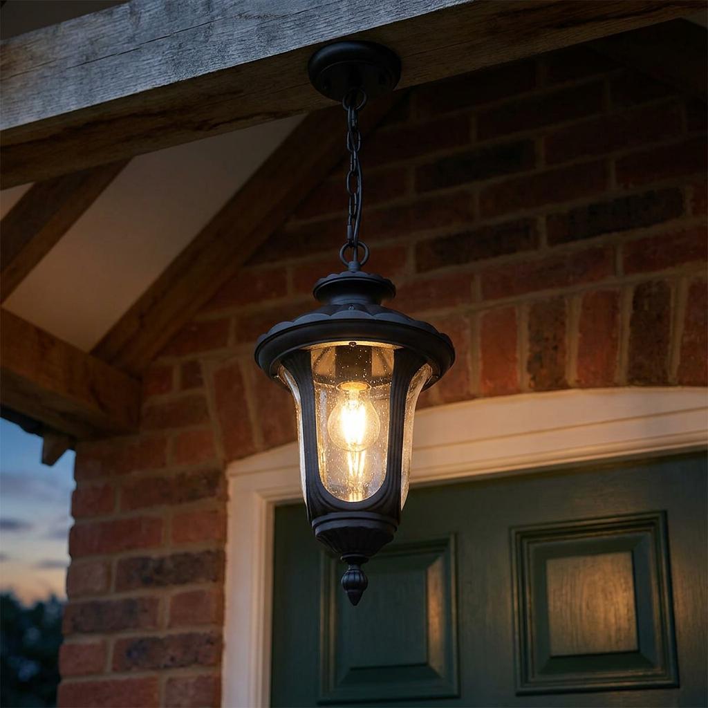Small black outdoor chain lantern with seeded glass shade lit up and hanging from a wooden porch beam.