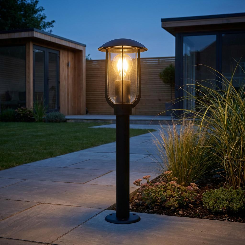 Modern black outdoor post light illuminating a grey tiled path in a contemporary garden at dusk.