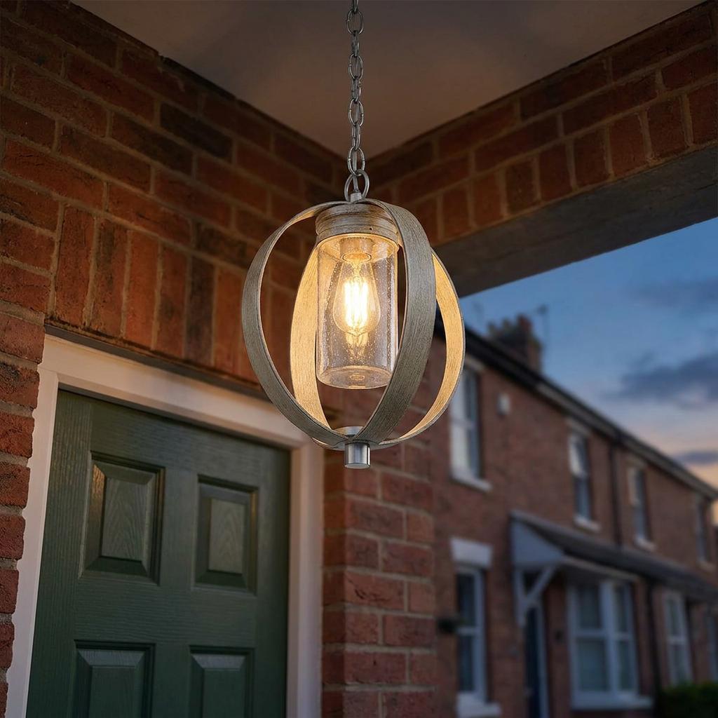 Rustic Grand Bank outdoor pendant with an orb frame and seeded glass cylinder hanging on a brick porch at dusk.