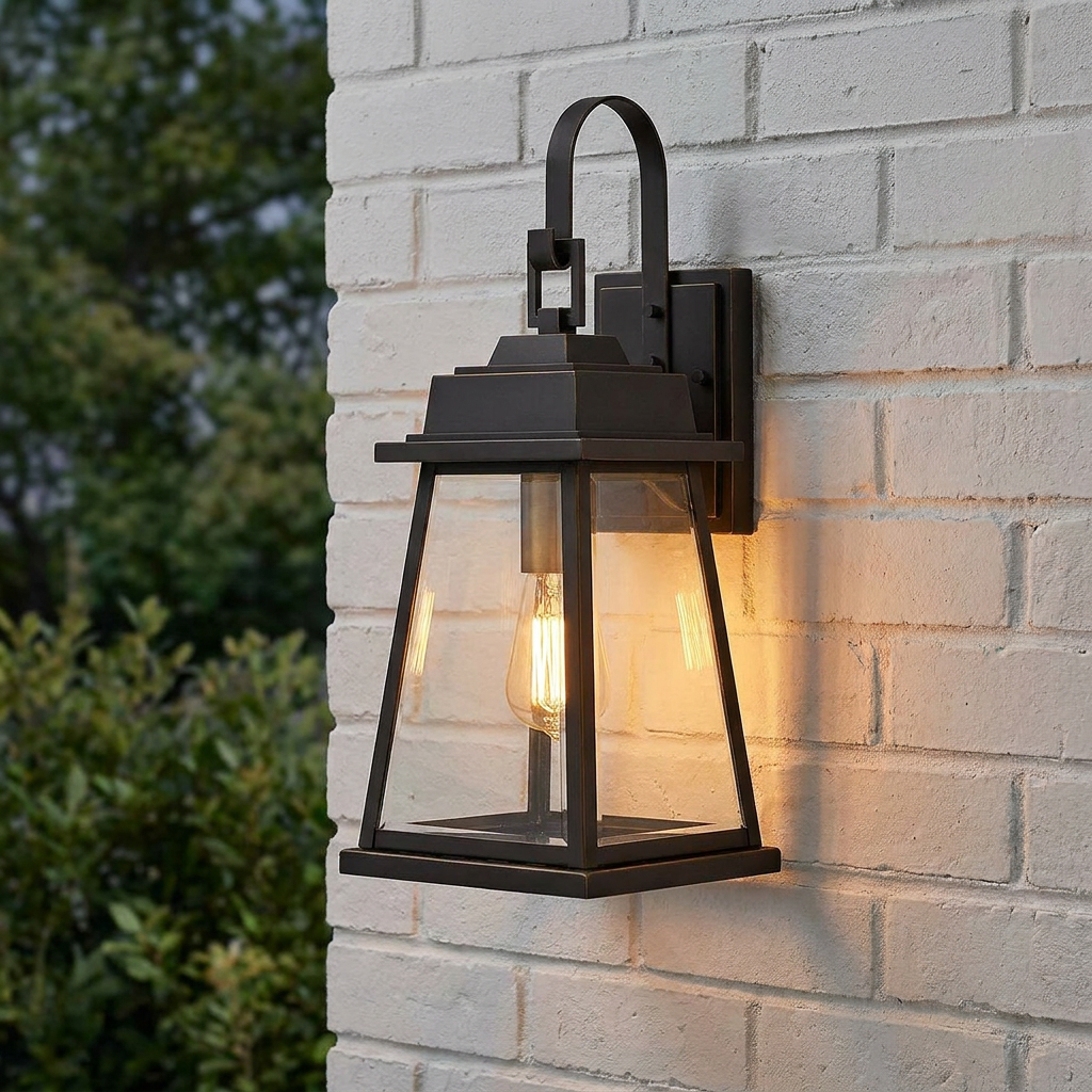 A bronze outdoor wall lantern with clear glass panes and a warm Edison bulb mounted on a white brick wall.