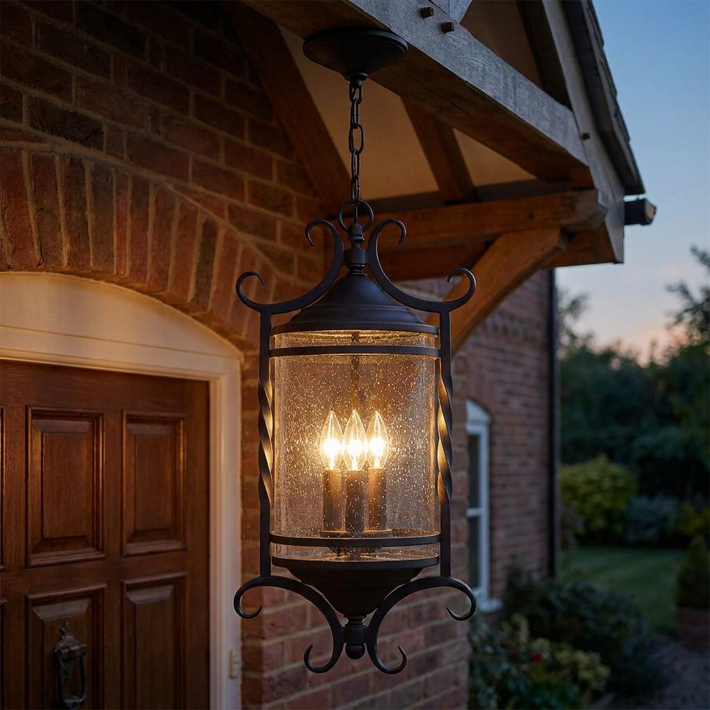 Ornate black outdoor chain lantern with seeded glass hanging from a wooden porch, illuminating a brick house at dusk.