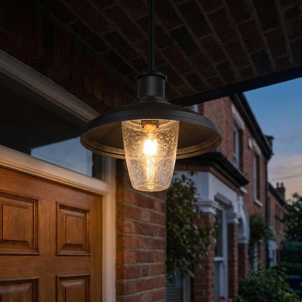 Black outdoor pendant light with a seeded glass shade hanging under a brick porch at sunset.